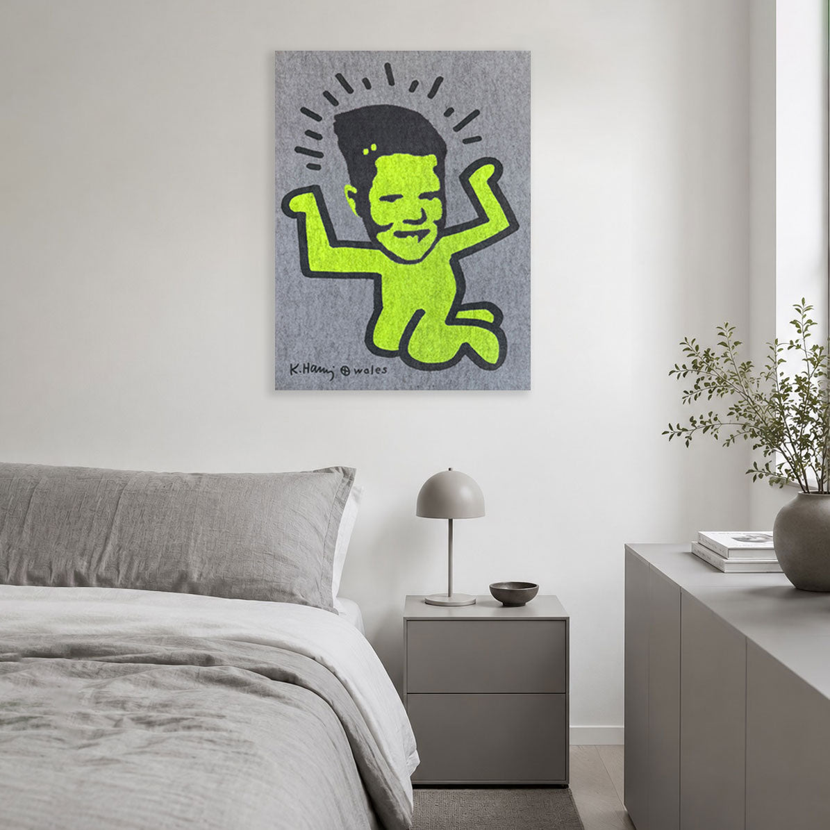 A canvas wall art print featuring a stylized neon green cartoon figure with black hair and facial features on a textured gray background, hanging on a white wall above a modern gray bed and nightstand in a minimalist bedroom.
