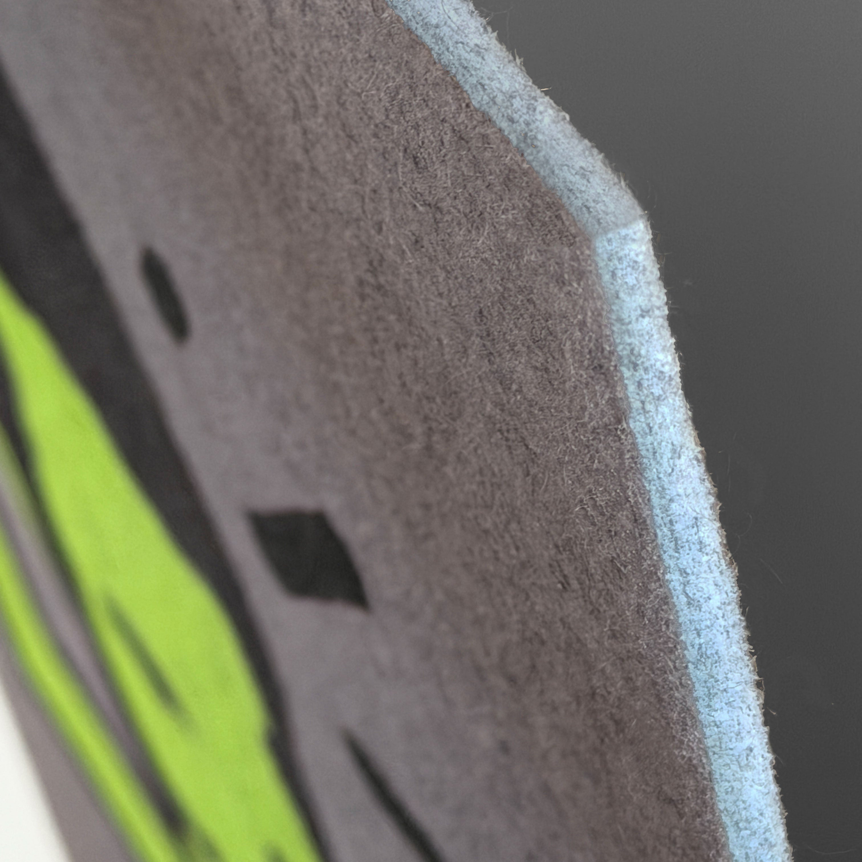 Close-up detail of a felt or fabric panel with a dark gray main body, a light blue backing edge, and a bright neon green graphic shape on a dark background.