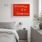 A framed wall art print with the phrase 'Breakfast of Champignons' in white handwritten text on a bright red background, displayed above a bed in a modern gray bedroom.
