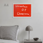 A framed wall art print with the phrase 'Breakfast of Champignons' in white handwritten text on a bright red background, shown hanging above a bed in a minimalist bedroom setting.