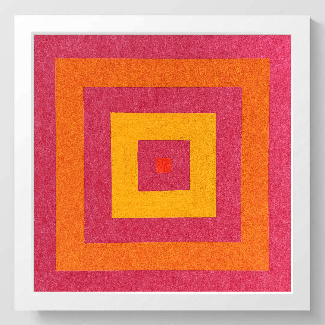 A square framed abstract art print featuring concentric geometric squares in bright pink, orange, and yellow on a textured background, set against a clean white wall.