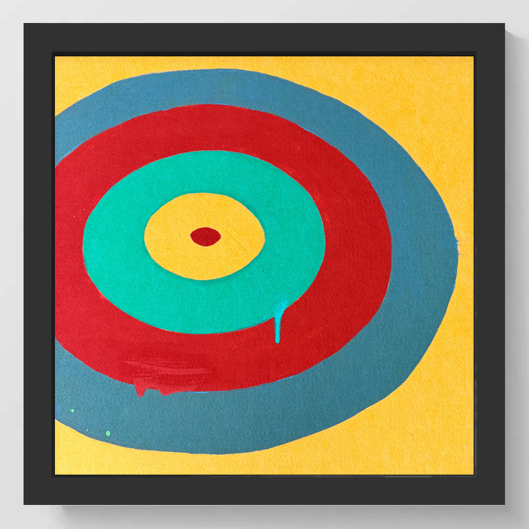 Framed abstract wall art featuring concentric circles in yellow, teal, red, and blue on a yellow background, shown in a black square frame against a light gray wall.