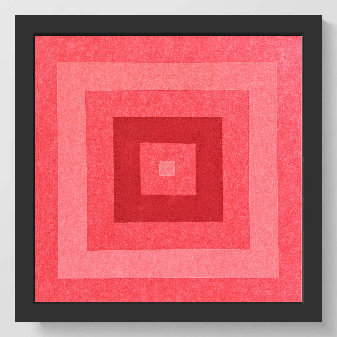 Framed square wall art featuring concentric squares in shades of coral, pink, and red, set in a thick black frame against a light gray wall.