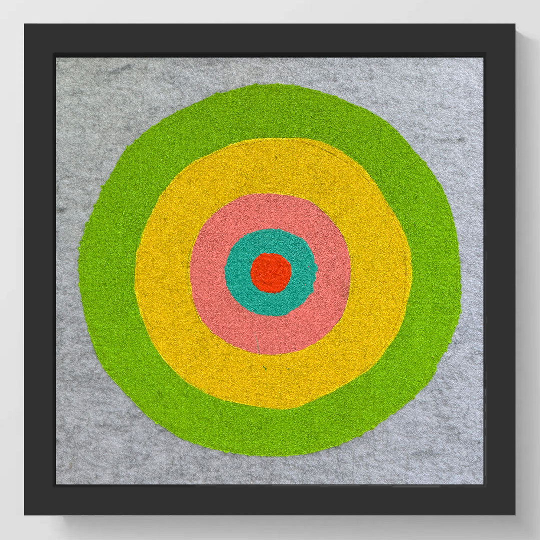 Framed square wall art featuring a hand-painted target design with concentric circles in green, yellow, pink, teal, and red on a textured gray background.