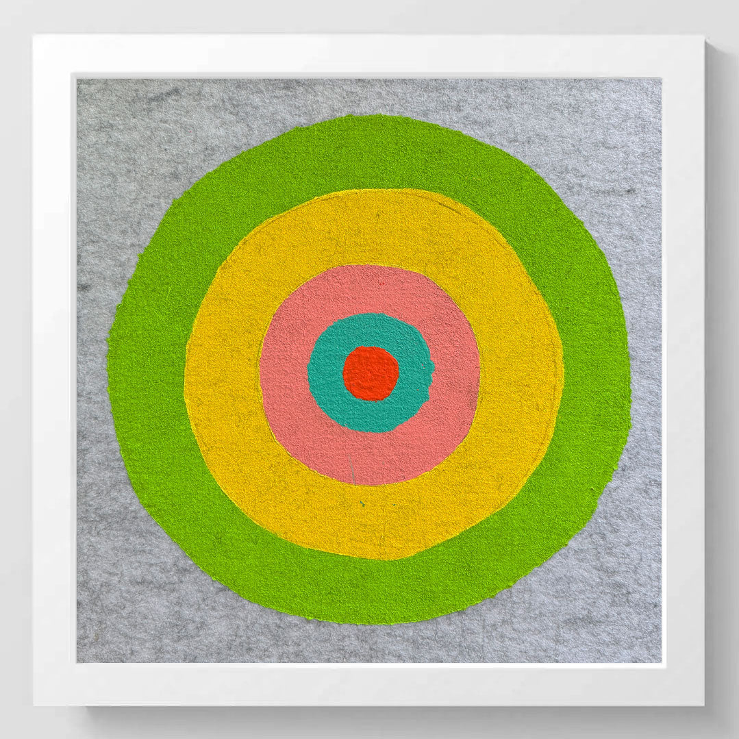 Framed square wall art featuring a colorful concentric target design with green, yellow, pink, teal, and red rings on a textured gray background, set in a white frame.