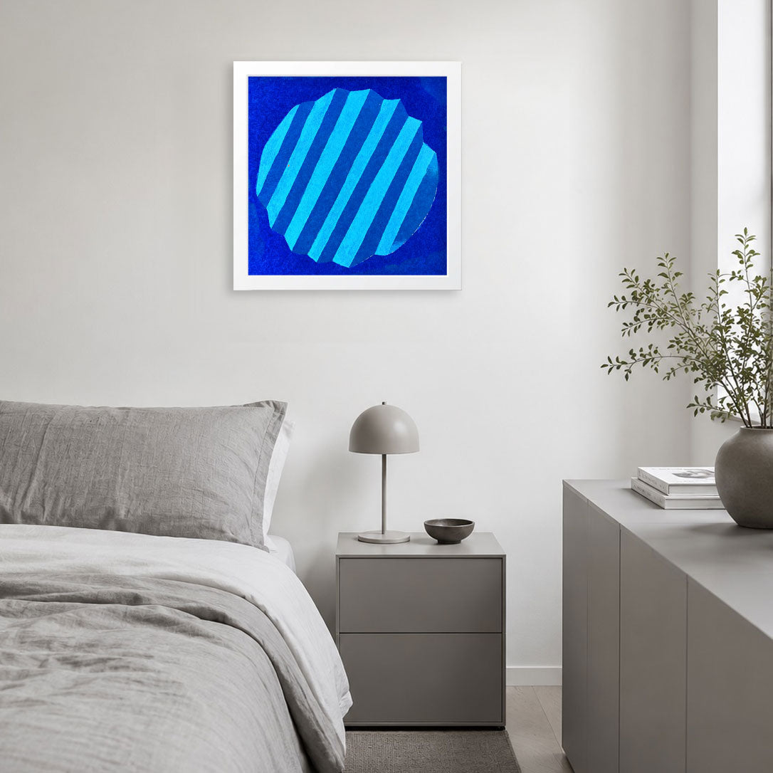 A framed abstract art print featuring a blue circular design with diagonal stripes, displayed on a light gray wall above a modern gray bed in a minimalist bedroom setting.