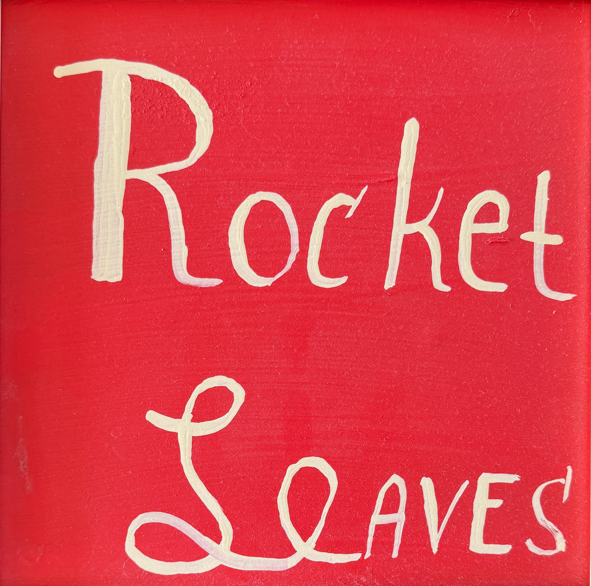 A square red painted canvas with the phrase 'Rocket Leaves' written in large white script across the front.